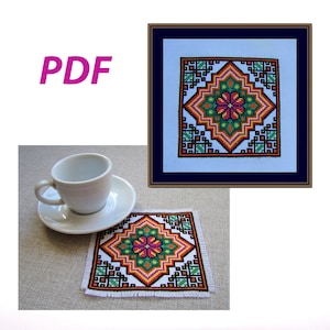 May include: A PDF pattern for a colorful cross stitch design featuring a geometric flower motif in shades of orange, yellow, green, pink, and black. The design is framed and shown on a coaster.