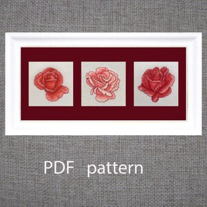 May include: A framed cross-stitch pattern featuring three red rose designs on a white background. The roses are set against a dark red backdrop within a white frame. The text "PDF pattern" is displayed below the frame.