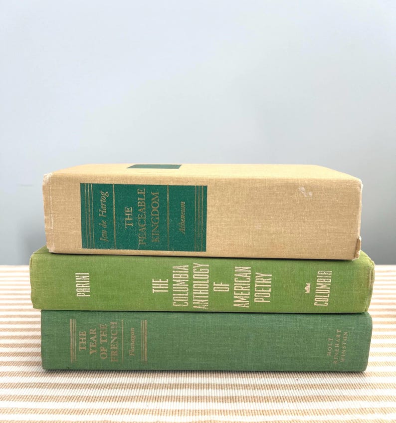 May include: Three stacked vintage books. The top book is beige with a green title label that reads "The Peaceable Kingdom." The middle book is green with "The Columbia Anthology of American Poetry." The bottom book is green with "The Year of the French."
