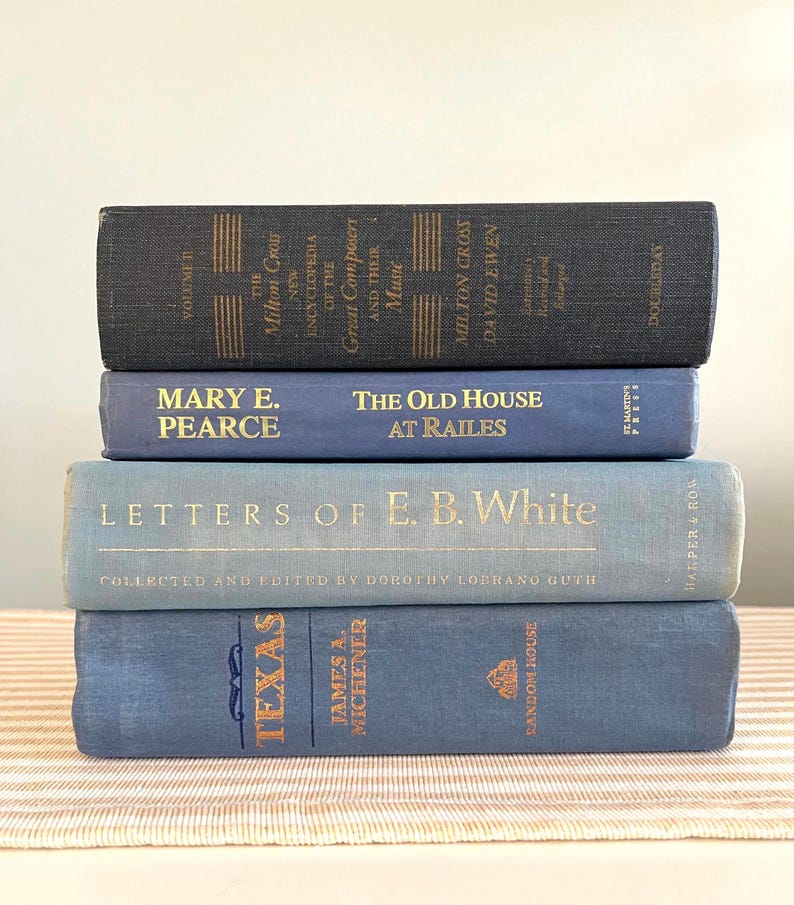 May include: A stack of four vintage books in shades of blue. The titles and authors are visible, including "Texas" by James A. Michener and "Letters of E. B. White." The books are arranged on a striped surface.