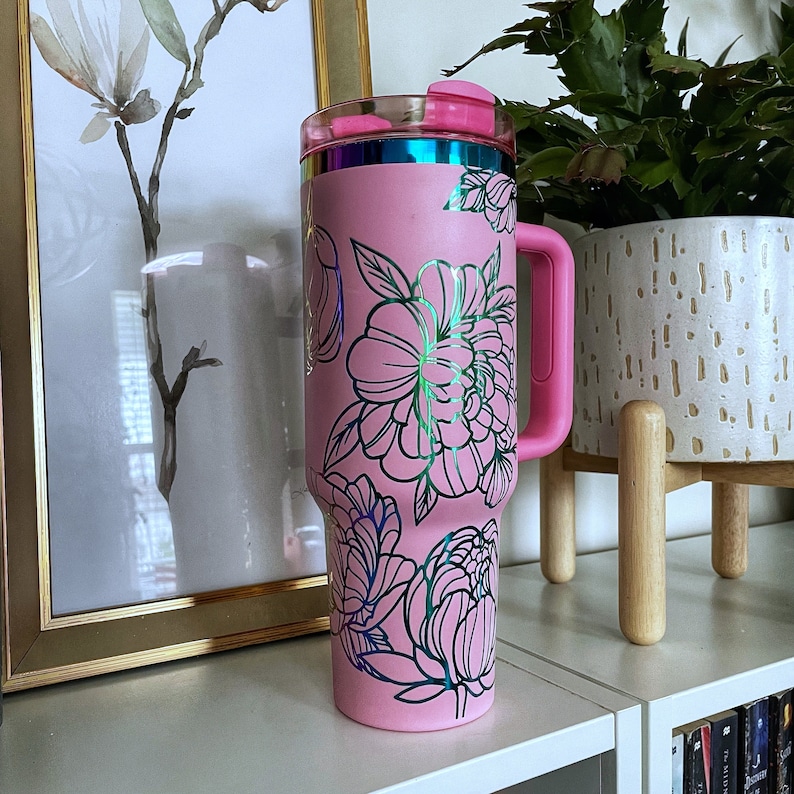 May include: Pink stainless steel tumbler with a floral design. The tumbler has a lid and a handle.