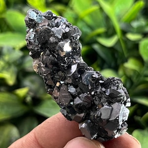 Puede incluir: Un cúmulo de cristales negros y plateados, con una superficie rugosa y texturizada. Los cristales están dispuestos en una forma irregular y dentada, que se asemeja a una pequeña cordillera.