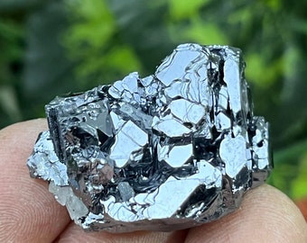 May include: A cluster of metallic gray crystals with a reflective surface. The crystals are arranged in a random pattern and have a sharp, angular shape.