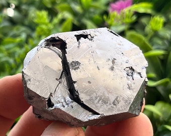 May include: A large, faceted, silver-colored crystal with a dark gray, almost black, interior. The crystal has a rough, natural texture and is irregularly shaped.
