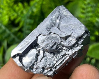 May include: A large, metallic gray, crystal with a rough, faceted surface. The crystal has a geometric shape and appears to be made of a single, large piece of mineral.