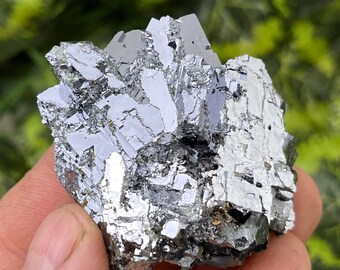 May include: A cluster of silver-colored crystals with a metallic sheen. The crystals are arranged in a jagged, irregular shape.