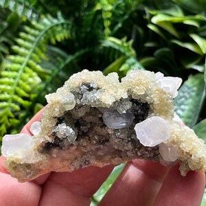 Puede incluir: Un cúmulo de cristales verdes y blancos con una textura rugosa y natural. Los cristales están dispuestos en un cúmulo, con algunos de los cristales apuntando hacia arriba y otros hacia abajo. Los cristales son translúcidos y tienen un ligero brillo.