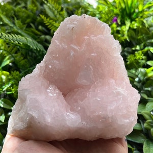 Puede incluir: Un gran cúmulo de cristal natural rosa con una superficie rugosa y texturizada. El cristal tiene una formación única en forma de cueva con un centro hueco.