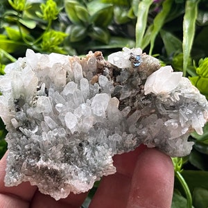 Puede incluir: Un cúmulo de cristales de cuarzo transparentes con una matriz mineral verde. Los cristales están agrupados en una formación natural rugosa.