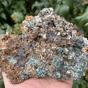 May include: A rough, gray rock with a cluster of shiny, metallic pyrite crystals. The rock is covered in small, turquoise-colored crystals.