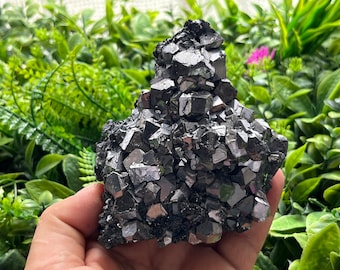 May include: A large cluster of black pyrite crystals with a metallic sheen. The crystals are arranged in a pyramid shape and have a rough, textured surface.