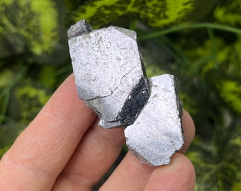 May include: A cluster of two silver-colored, metallic, geometrically shaped crystals. The crystals have a rough, textured surface.