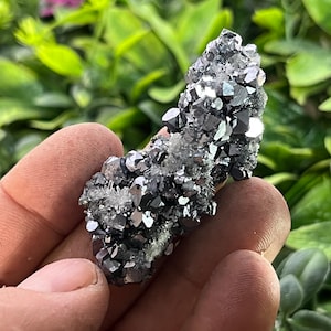 Puede incluir: Un cúmulo de cristales plateados y negros con un brillo metálico. Los cristales están dispuestos en un patrón aleatorio y tienen una variedad de formas y tamaños.