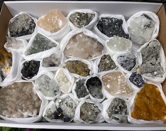 May include: A collection of various crystals and minerals, including quartz, pyrite, and calcite, displayed in individual white pouches. The crystals are arranged in a box, showcasing their natural beauty and unique formations.