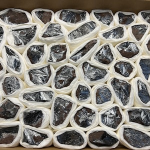 May include: A box filled with wrapped silver and black crystals. The crystals are wrapped in white tissue paper and are arranged in a grid pattern.