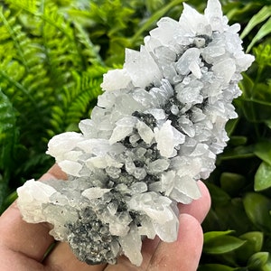 Puede incluir: Un cúmulo de cristales de calcita blancos con una base metálica gris. Los cristales están dispuestos en una formación en forma de abanico en capas.