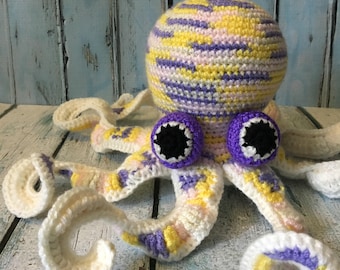 May include: A crocheted octopus toy with a white, yellow, and purple striped body and black eyes. The octopus has eight tentacles.