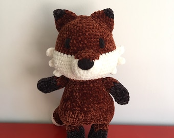 May include: A plush fox toy made of brown, white, and black velvet yarn. The fox features a white muzzle, dark brown ears, black paws, and a dark brown nose. The stuffed animal has a soft, textured appearance with visible crochet stitches throughout.