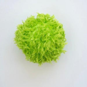 May include: A spherical pom-pom crafted from vibrant lime green eyelash yarn. The texture is fuzzy and feathery, with numerous thin, wispy strands radiating outward from the center to create a dense, rounded shape with a bright, solid color.