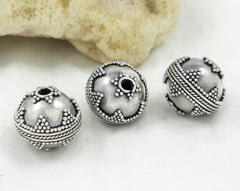 May include: Three silver beads with intricate designs. The beads are round and have a hole in the center for stringing. The beads are made of metal and have a shiny finish.