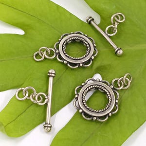 May include: Four silver-toned toggle clasps with ornate circular designs. Each clasp has a decorative ring and a bar with a small ball at the end.
