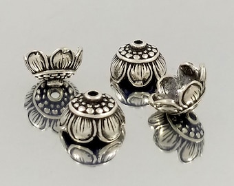 May include: Silver-toned metal bead caps with a floral design. The caps have a round base and a scalloped top.