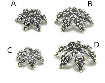 May include: Four silver-toned metal bead caps with a flower design. Each cap has a different shape and size.