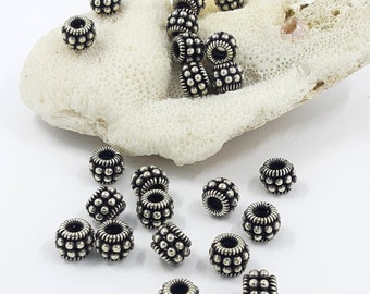 May include: A collection of silver-toned metal beads with a textured, raised dot pattern. The beads are scattered on a white surface.