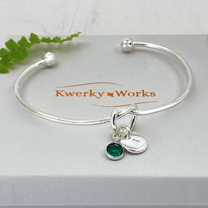 Personalised Silver Knot Bracelet with Initial and Birthstone Crystal: Meaningful Jewellery Gift for Women. This beautiful silver plated, open cuff, friendship knot bracelet makes a perfect gift for family or friend. It can be personalised with a birthstone crystal charm and a silver-plated initial letter charm of your choice. Here it is seen placed on top of the eco-friendly gift box that is included.