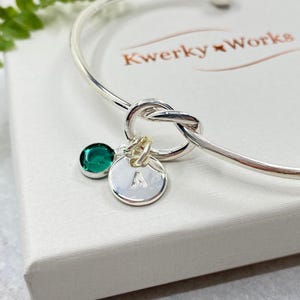 This image shows a close-up detail shot of the bracelet showing the knot, the May (Emerald Crystal) birthstone and a small round silver-plated initial letter charm, imprinted with a letter A.