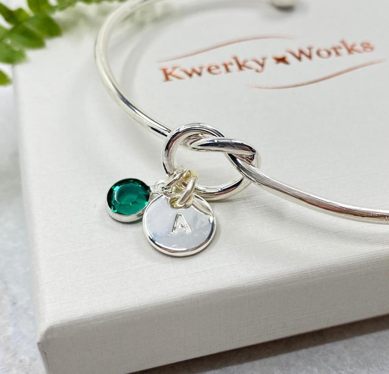 This image shows a close-up detail shot of the bracelet showing the knot, the May (Emerald Crystal) birthstone and a small round silver-plated initial letter charm, imprinted with a letter A.