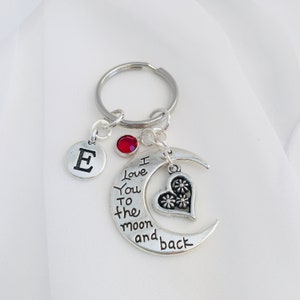 May include: Silver keyring with a crescent moon charm that says "I love you to the moon and back". The charm also has a small heart with floral details. The keyring also has a silver letter "E" charm and a red rhinestone.