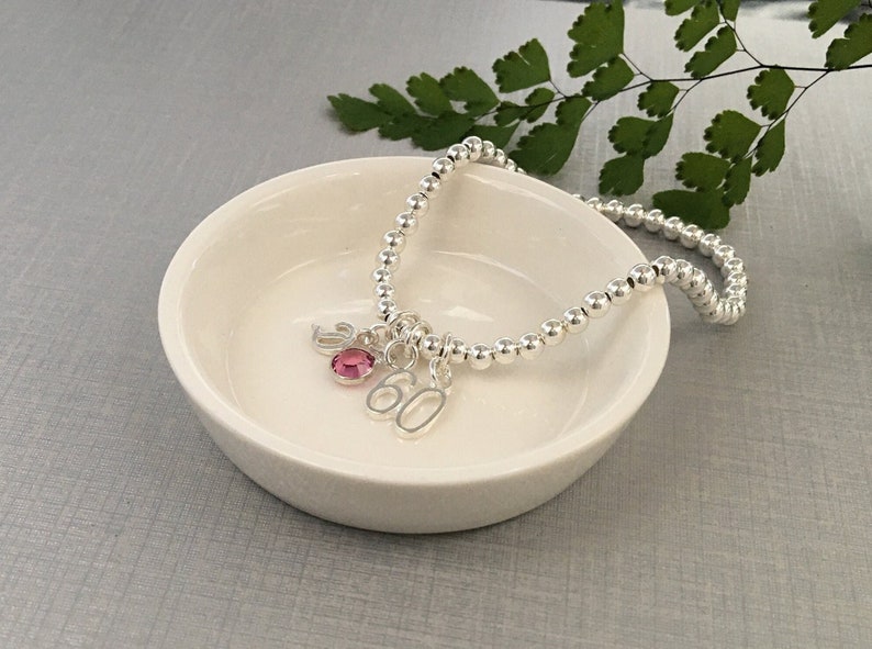 Personalised 60th Birthday Gift for women - sterling silver beaded stacking bracelet with birthstone crystal, sterling silver Initial and silver-plated age number charm. The bracelet is made using jewellers elastic for ease of putting on and removal.