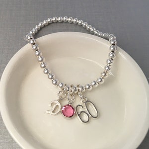 Sterling silver beaded stretch bracelet with birth-month crystal, letter tag and special age charm. Select your favourite crystal colour or the one that corresponds to your birth month. Choose from 12 colours and 26 script initial charms.