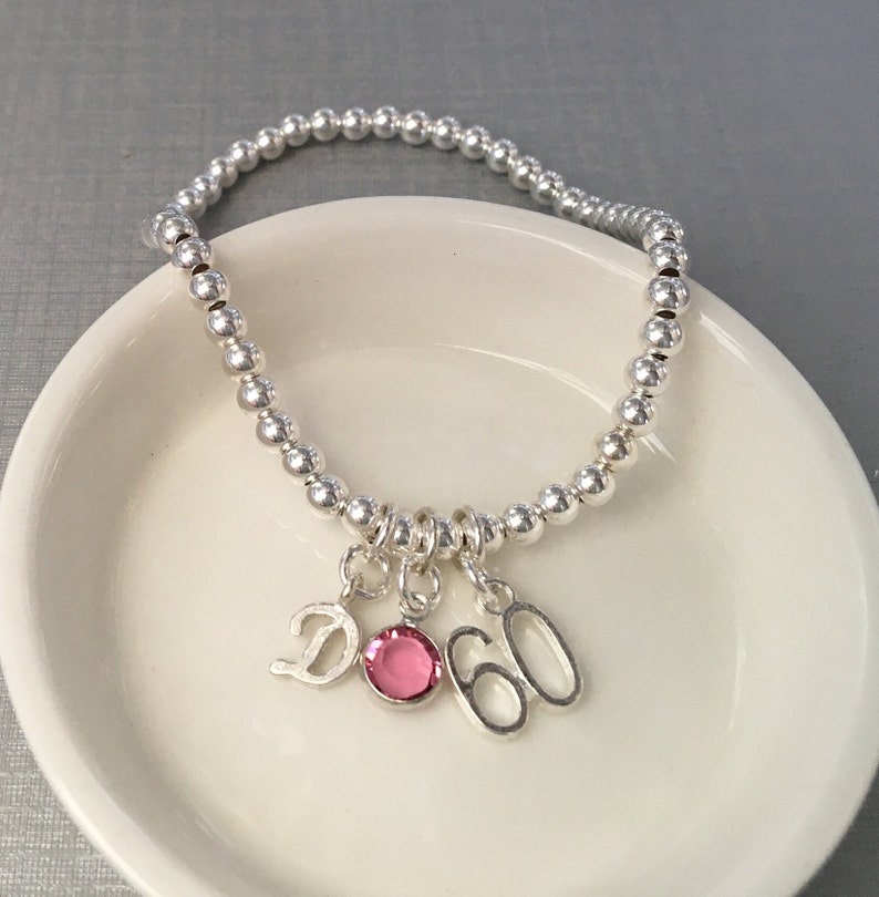 Sterling silver beaded stretch bracelet with birth-month crystal, letter tag and special age charm. Select your favourite crystal colour or the one that corresponds to your birth month. Choose from 12 colours and 26 script initial charms.