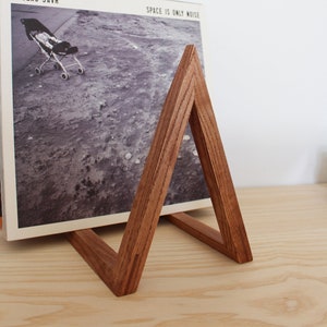 May include: A wooden record stand in the shape of a triangle, holding a vinyl record with the album title "Space is Only Noise" by Nicolas Jaar.