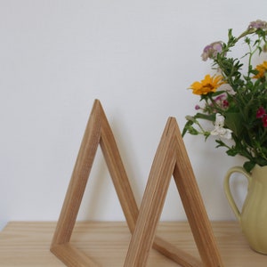 May include: A wooden triangle shelf unit made of light brown wood. The shelf unit is made of two triangles that are joined together at the base. The shelf unit is sitting on a light brown wooden surface.