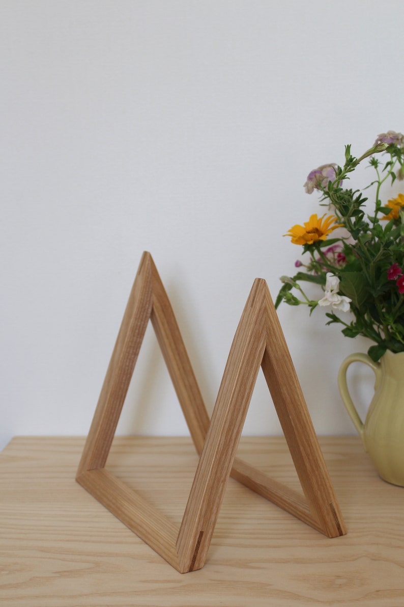 May include: A wooden triangle shelf unit made of light brown wood. The shelf unit is made of two triangles that are joined together at the base. The shelf unit is sitting on a light brown wooden surface.