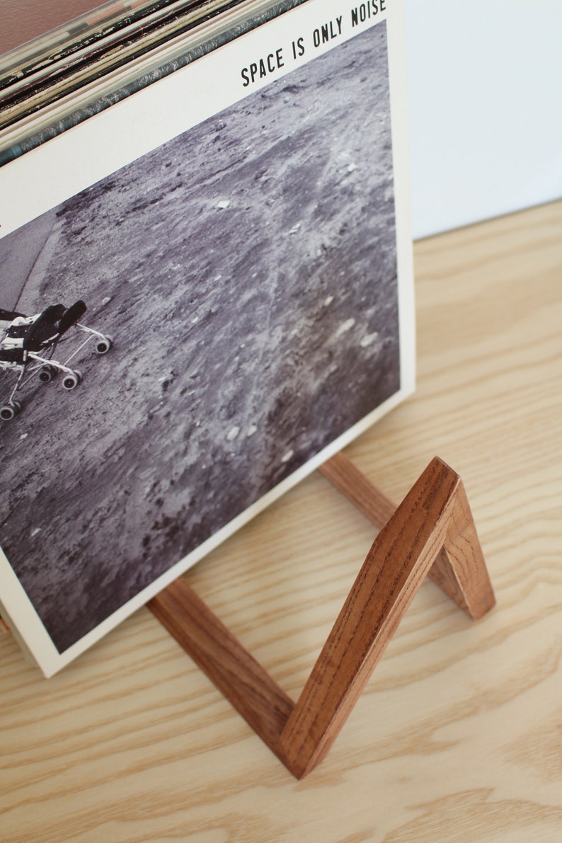 May include: A wooden record stand with a dark brown stain. The stand is holding a vinyl record with the text "SPACE IS ONLY NOISE" on the cover.