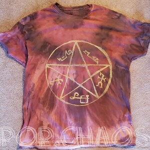 May include: A tie-dye t-shirt in shades of red, pink, and brown, featuring a gold-colored pentagram design in the center. The text "POP CHAOS" is visible at the bottom of the shirt.