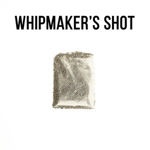 Op de afbeelding: Een doorzichtige plastic zak gevuld met kleine, zilveren metalen ballen. De zak is gelabeld met "WHIPMAKER'S SHOT".