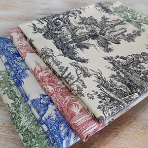 May include: A stack of folded fabric with a toile pattern in green, blue, red, and black. The fabric features a cream background with detailed illustrations of landscapes and figures. The folded edges of the fabric are visible, showcasing the different color variations.