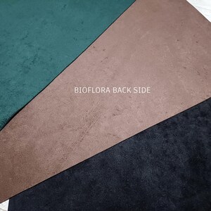 May include: A close-up of three fabric samples in green, brown, and black. The green is a dark, forest hue, the brown is a muted tan, and the black is a deep tone. The text "BIOFLORA BACK SIDE" is printed in white across the image.