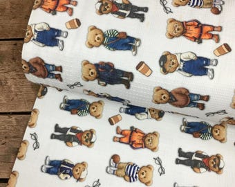 May include: A white waffle-knit fabric featuring a repeating pattern of brown teddy bears dressed in various outfits, including hoodies, vests, and overalls, interspersed with small illustrations of coffee cups and eyeglasses.