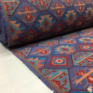 May include: A roll of patterned fabric with a geometric design in shades of blue, red, orange, and teal. The fabric features a repeating pattern of diamond and geometric shapes. The edges are finished with a brown trim and fringe.