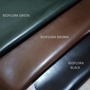 May include: Close-up of three leather swatches in green, brown, and black. The text "BIOFLORA GREEN", "BIOFLORA BROWN", and "BIOFLORA BLACK" are printed on the swatches. The leather has a smooth, shiny finish.
