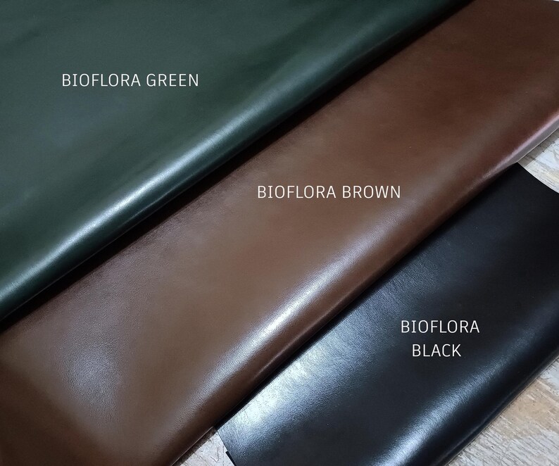 May include: Close-up of three leather swatches in green, brown, and black. The text "BIOFLORA GREEN", "BIOFLORA BROWN", and "BIOFLORA BLACK" are printed on the swatches. The leather has a smooth, shiny finish.
