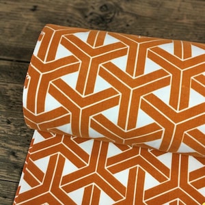 May include: Close-up of a folded fabric roll featuring a repeating geometric pattern. The design consists of interconnected orange and white shapes, creating a visually striking and modern aesthetic. The fabric appears to be cotton or a similar material, suitable for various crafting projects.