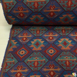 May include: A roll of patterned fabric featuring a geometric design in shades of blue, red, orange, and teal. The repeating pattern includes diamond shapes and stylized motifs, with a textured appearance. The fabric has a brown edge.