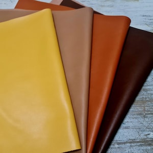 May include: A selection of leather swatches in warm shades. The colours range from yellow to brown, including tan and orange. The leather has a smooth surface and a subtle sheen, indicating a high-quality material for crafting.